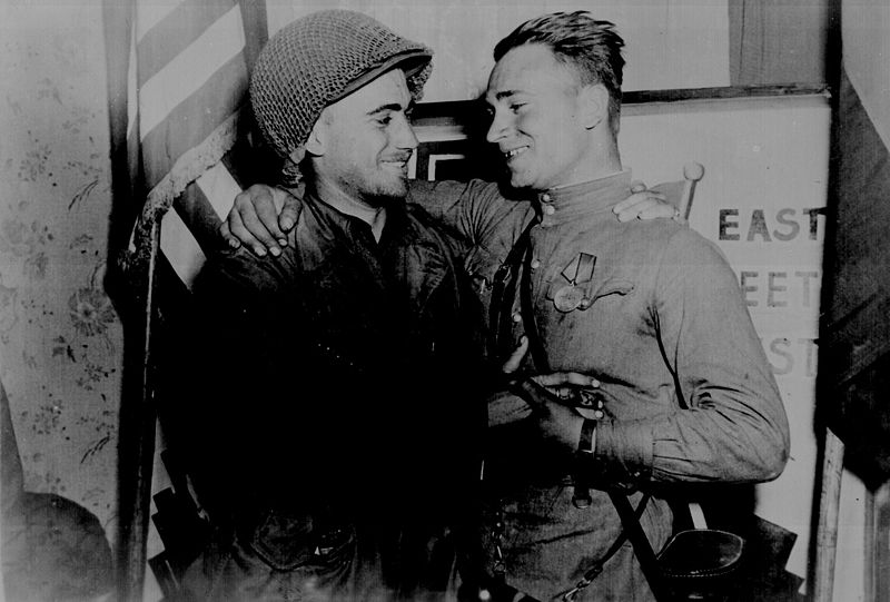 Счастливые 2-й лейтенант У. Робертсон и лейтенант А. С. Сильвашко на фоне надписи «Восток встречается с Западом», символизирующей историческую встречу союзников на Эльбе.